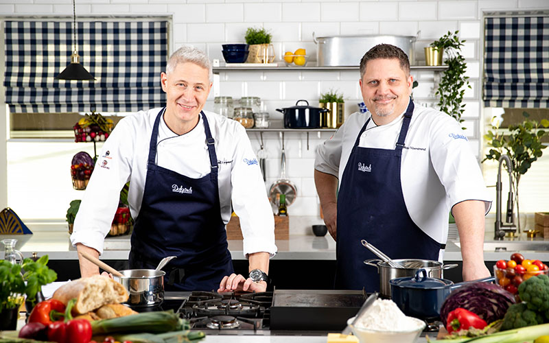 Bild på två killar i kockkläder som står i ett kök